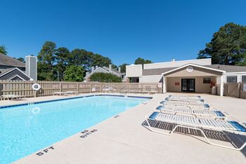 A pool with sun loungers and a building in the background.